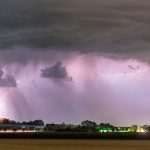 Bright lightning forks through dark storm clouds across a dramatic night sky.