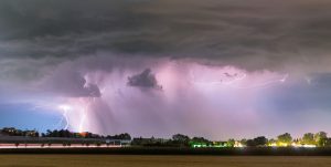 Bright lightning forks through dark storm clouds across a dramatic night sky.
