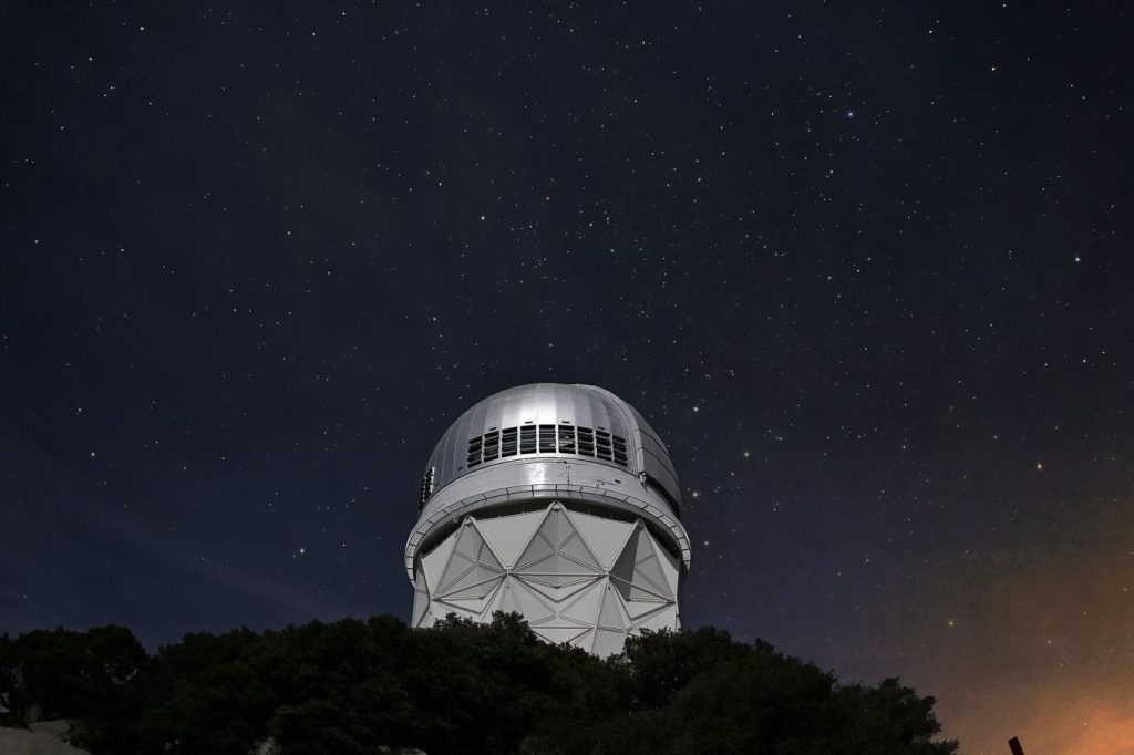 A telescope at an observatory silhouetted against a clear night sky filled with stars.