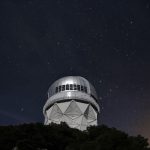 A telescope at an observatory silhouetted against a clear night sky filled with stars.