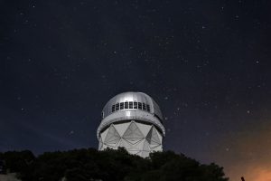 A telescope at an observatory silhouetted against a clear night sky filled with stars.